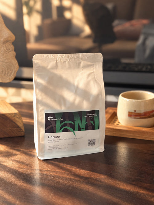 Amarelo Garapa whole-bean coffee bag beside a ceramic cup in warm sunlight