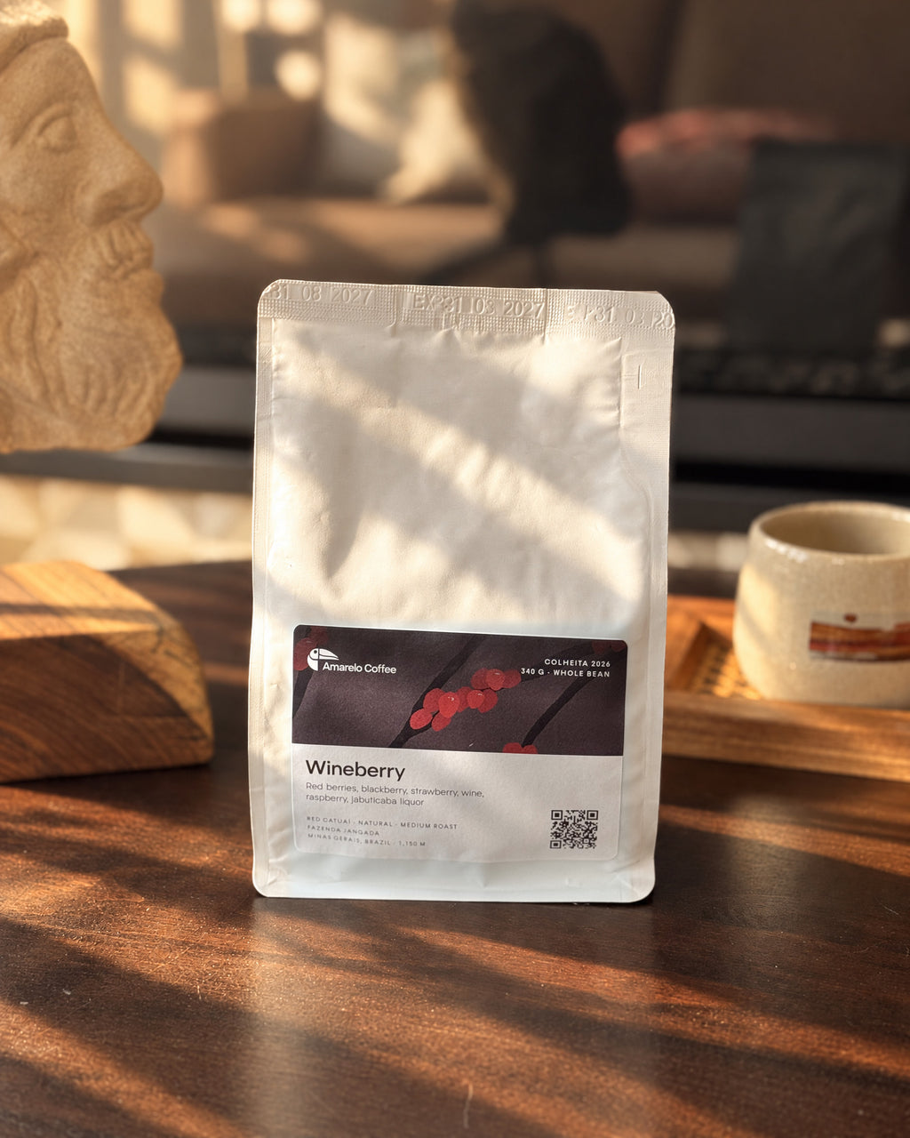 Amarelo Wineberry whole-bean coffee bag beside a ceramic cup in warm sunlight
